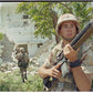 Jarrett holding a rifle in a combat zone "Somalia" with other soldiers in the background.